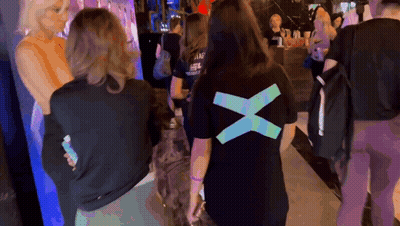 A Woman Wearing A Black T-Shirt With A Blue X On The Back GIF
