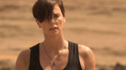 A Woman Wearing A Black Tank Top And A Necklace With A Pendant On It GIF