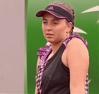 A Woman Wearing A Black Tank Top And A Purple Visor Is Standing In Front Of A Green Wall . GIF