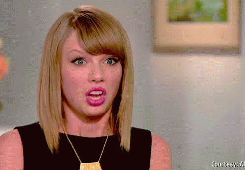 A Woman Wearing A Black Top And A Gold Necklace Is Making A Surprised Face GIF