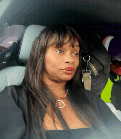 A Woman Wearing A Black Top And A Gold Necklace Is Sitting In The Back Seat Of A Vehicle GIF