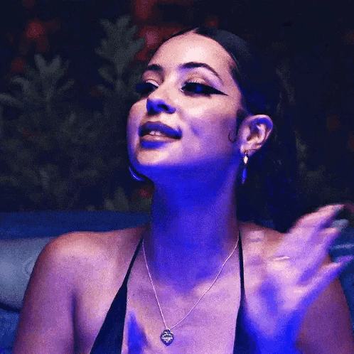 A Woman Wearing A Black Top And A Necklace Is Waving Her Hand In The Dark . GIF