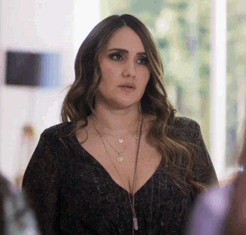 A Woman Wearing A Black Top And A Necklace With A Pendant That Says ' U ' On It GIF