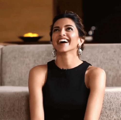 A Woman Wearing A Black Top And Earrings Is Laughing GIF