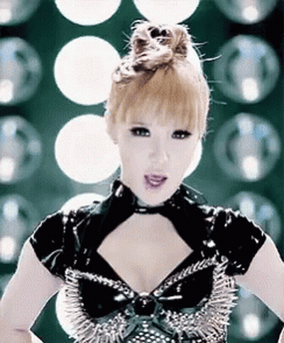 A Woman Wearing A Black Top With Spikes On It Is Standing In Front Of A Bunch Of Lights . GIF