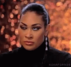 A Woman Wearing A Black Turtleneck And Earrings Is Making A Silly Face . GIF