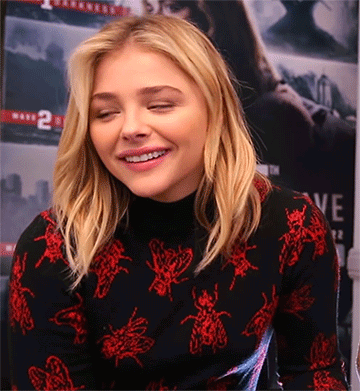 A Woman Wearing A Black Turtleneck With Red Bees On It GIF