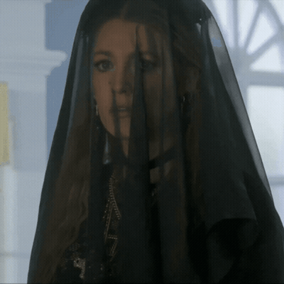 A Woman Wearing A Black Veil Is Standing In Front Of A Window GIF