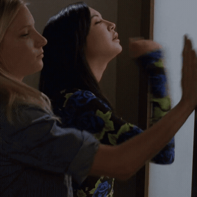 A Woman Wearing A Blue And Green Floral Top Looks Out A Window GIF
