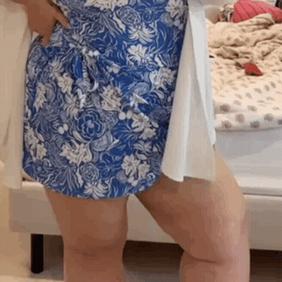 A Woman Wearing A Blue And White Floral Dress Is Standing In Front Of A Bed . GIF