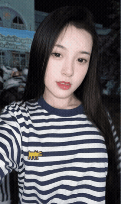 A Woman Wearing A Blue And White Striped Shirt Takes A Selfie With Her Phone GIF