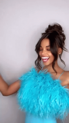 A Woman Wearing A Blue Feathered Top Is Laughing And Dancing . GIF