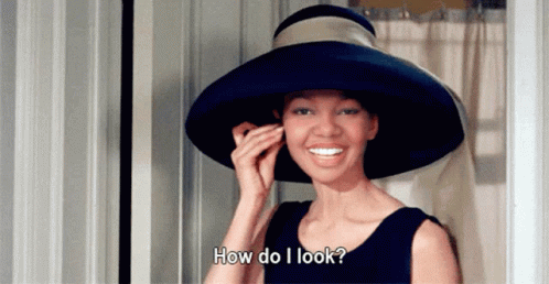 A Woman Wearing A Blue Hat Is Smiling And Asking How Do I Look GIF