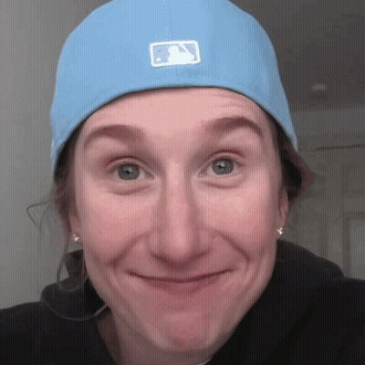 A Woman Wearing A Blue Hat With A Baseball Logo On It Makes A Funny Face GIF