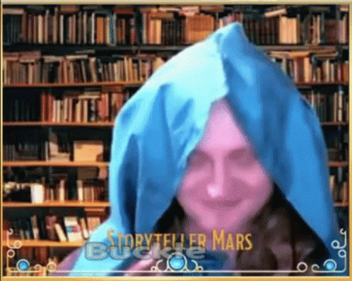 A Woman Wearing A Blue Hooded Cape Is Standing In Front Of A Bookshelf . GIF