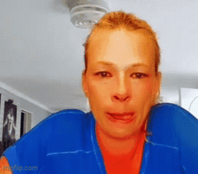 A Woman Wearing A Blue Jacket And An Orange Shirt Is Looking At The Camera GIF