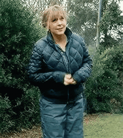 A Woman Wearing A Blue Jacket And Blue Pants Is Standing In Front Of Trees . GIF