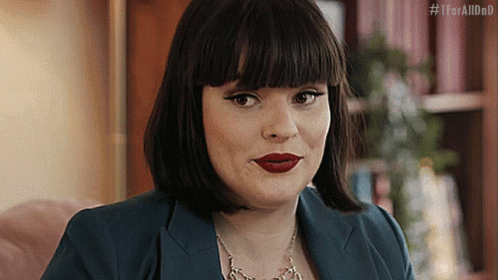 A Woman Wearing A Blue Jacket And Red Lipstick Is Sitting On A Pink Couch . GIF