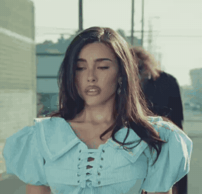 A Woman Wearing A Blue Lace Up Top Is Standing On A Sidewalk . GIF