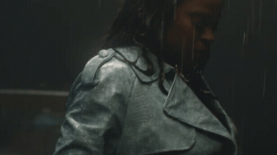A Woman Wearing A Blue Leather Jacket Is Standing In The Rain GIF