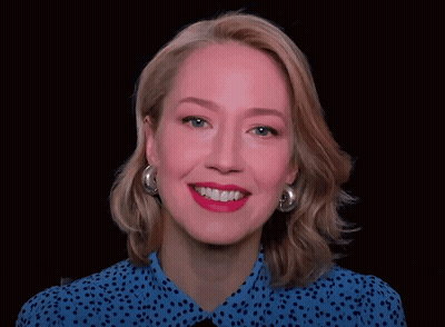 A Woman Wearing A Blue Polka Dot Shirt And Silver Hoop Earrings Is Smiling GIF