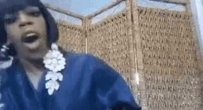 A Woman Wearing A Blue Robe And Earrings Is Standing In Front Of A Wicker Screen . GIF