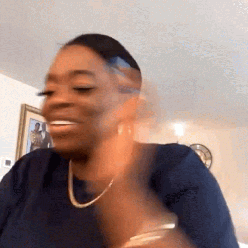 A Woman Wearing A Blue Shirt And A Necklace Is Smiling In A Room . GIF