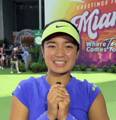 A Woman Wearing A Blue Shirt And A Yellow Nike Visor Smiles In Front Of A Miami Sign GIF