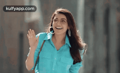 A Woman Wearing A Blue Shirt And Hoop Earrings Is Waving Her Hand . GIF