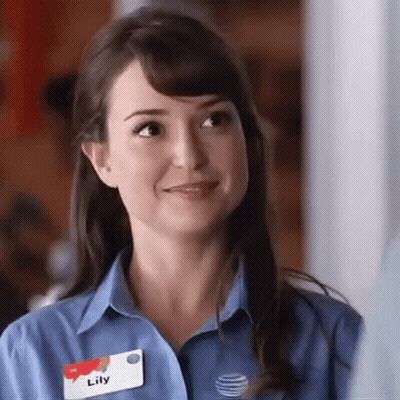 A Woman Wearing A Blue Shirt And Name Tag Is Smiling . GIF