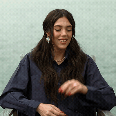 A Woman Wearing A Blue Shirt And Pearls Is Sitting In A Chair GIF