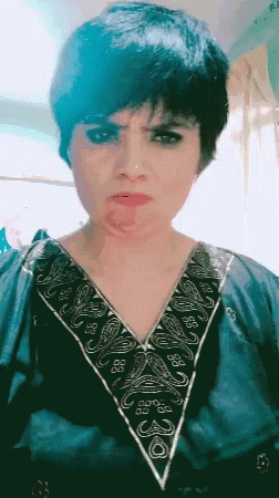 A Woman Wearing A Blue Shirt With A Floral Embroidery On The Collar Looks At The Camera GIF