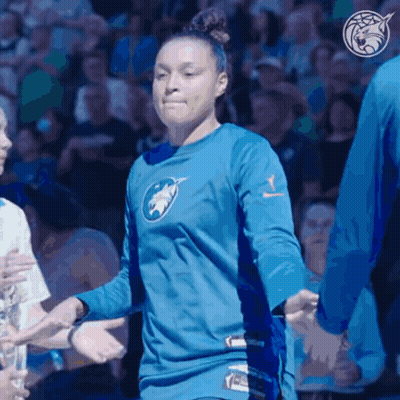 A Woman Wearing A Blue Shirt With A Wolf On It Shakes Hands With Other People GIF
