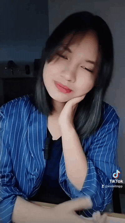 A Woman Wearing A Blue Striped Shirt Is Sitting At A Table With Her Hand On Her Chin . GIF