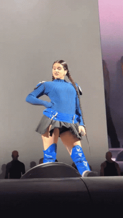 A Woman Wearing A Blue Sweater And Blue Boots Is Standing On A Stage GIF