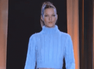 a woman wearing a blue sweater is standing in front of a black curtain .
