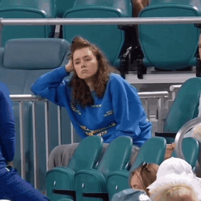 A Woman Wearing A Blue Sweatshirt That Says Silk Mills Sits In A Stadium GIF