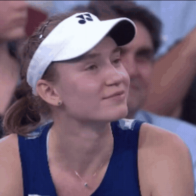 A Woman Wearing A Blue Tank Top And A White Visor Is Smiling While Sitting In A Crowd . GIF
