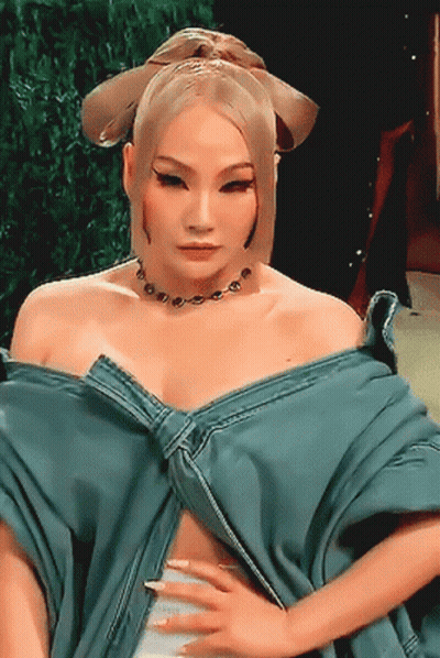 A Woman Wearing A Blue Top And A Necklace Is Looking At The Camera GIF