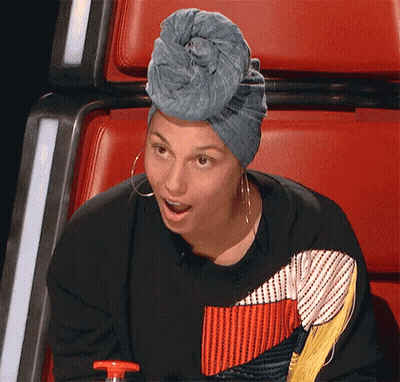 A Woman Wearing A Blue Turban And Earrings Is Sitting In A Red Chair . GIF
