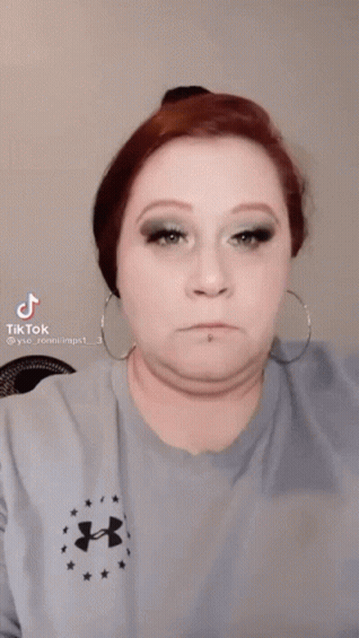 A Woman Wearing A Blue Under Armour Shirt Is Applying Makeup To Her Eye . GIF