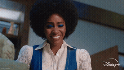 A Woman Wearing A Blue Vest And White Shirt Is Smiling For Disney + GIF