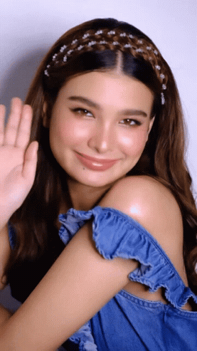 A Woman Wearing A Braided Headband Is Smiling And Waving Her Hand GIF
