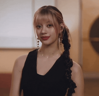 A Woman Wearing A Braided Ponytail And Earrings Is Looking At The Camera GIF