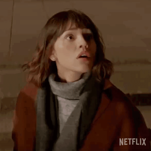 Woman In Brown Coat And Gray Sweater Standing In Dark Room GIF