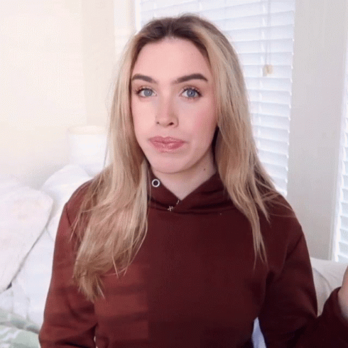 A Woman Wearing A Brown Hoodie Is Making A Silly Face GIF