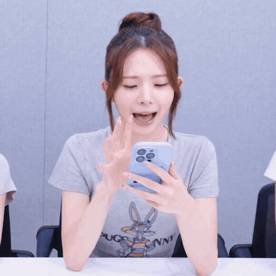 A Woman Wearing A Bugs Bunny Shirt Is Holding A Cell Phone In Her Hand GIF