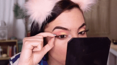 A Woman Wearing A Cat Ear Headband Is Applying Eye Shadow To Her Eye . GIF