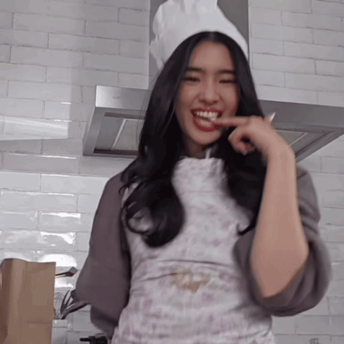 A Woman Wearing A Chef 'S Hat And Apron Is Smiling In A Kitchen GIF