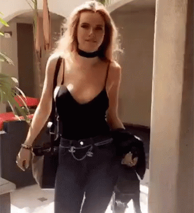 A Woman Wearing A Choker And A Black Tank Top Is Walking Down A Sidewalk . GIF